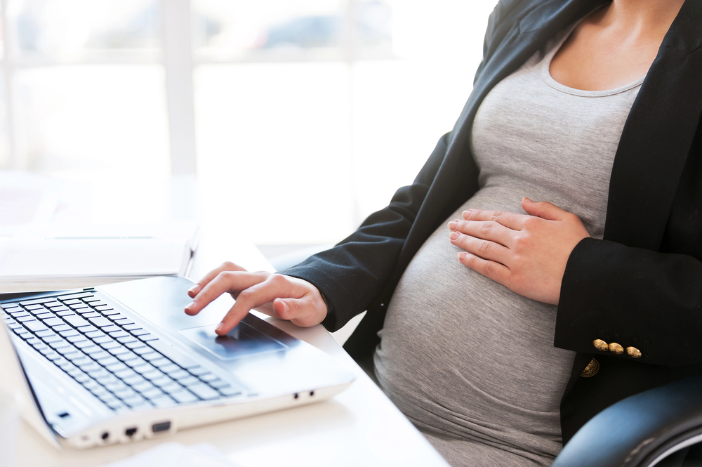 Pregnant worman working, contacting a pregnancy discrimination lawyer.